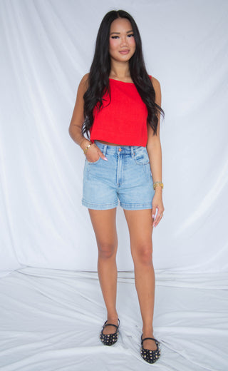 Woman wearing a red top and light blue shorts against a white background