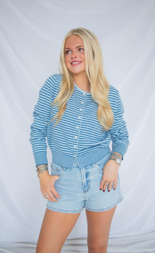 Woman wearing a blue striped shirt and denim shorts against a plain background
