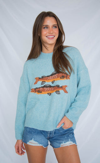 Woman wearing a light blue sweater with fish designs on a plain background