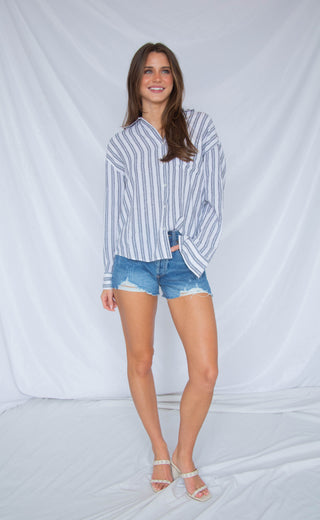 Woman wearing a striped button down shirt and denim shorts against a white background