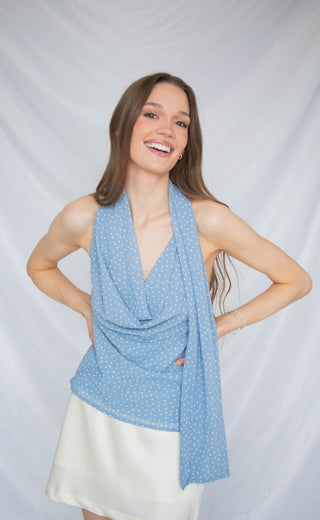 Woman wearing a blue polka dot scarf cowl neck top against a plain background