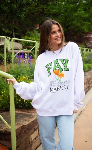 Woman wearing a white sweatshirt with 'FAY' and 'Farmer's Market' text, standing outdoors.