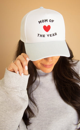 Woman  wearing a striped trucker hat with 'Mom of the Year' text and red heart on beige background