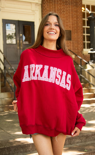 Person wearing a red 'ARKANSAS ' sweatshirt in front of a building.