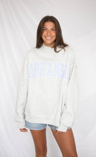 Woman wearing a light gray sweatshirt with 'ARKANSAS' text on a white background