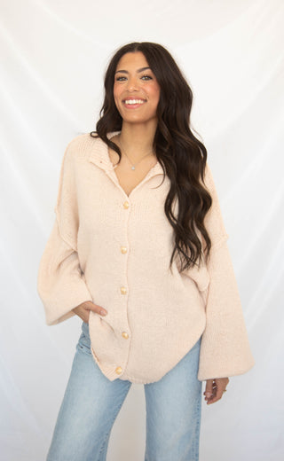 Woman wearing a light pink cardigan with light blue jeans on a white background