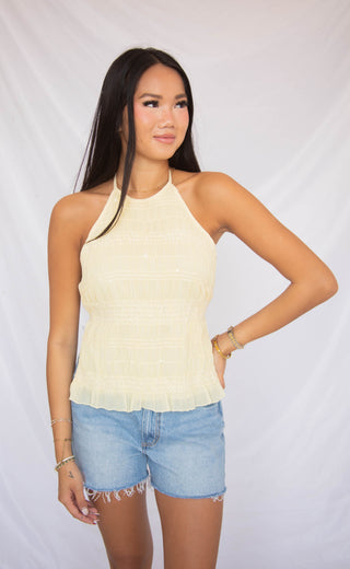 Woman wearing a light yellow halter top and denim shorts against a plain background