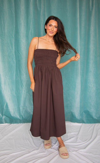 Woman wearing a brown midi dress against a teal curtain background