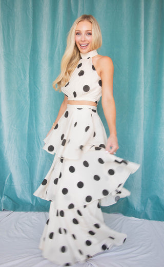 Woman wearing a black and white polka dot two piece set against a light blue curtain background