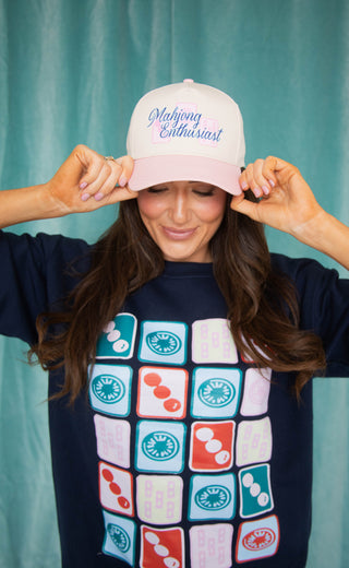 Person wearing a navy sweatshirt with Mahjong-themed design and a white cap with text.