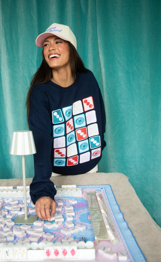 Person wearing a navy sweatshirt with colorful square patterns, sitting at a table with a board game.