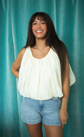 Woman wearing a white top and blue shorts against a teal curtain background