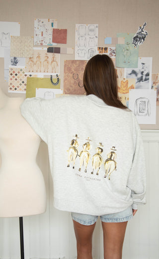 Person wearing a light gray sweatshirt with a graphic design, standing in front of a wall with various drawings and notes.