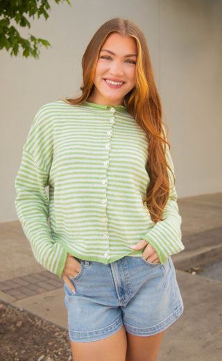 Woman wearing a green striped cardigan and denim shorts standing outdoors.