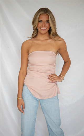 Women wearing light pink strapless tube top with ruching details. 