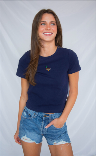 Woman wearing a navy blue t-shirt with a small mallard duck embroidery on a plain background