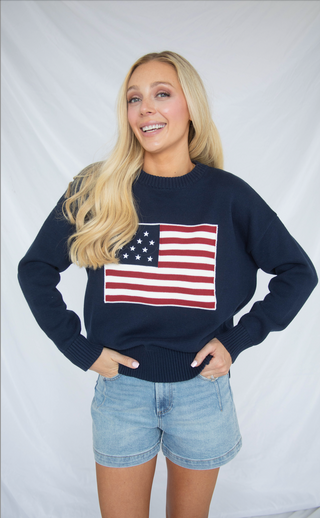 Woman wearing a navy sweater with an American flag design against a white background