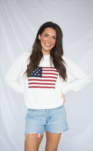 Woman wearing a white sweatshirt with an American flag design on a plain background