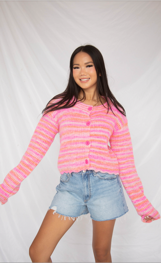 Person wearing a pink and orange striped sweater with denim shorts on a white background