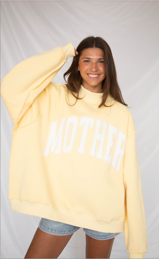 Person wearing a light yellow sweatshirt with 'MOTHER' printed on it against a plain background