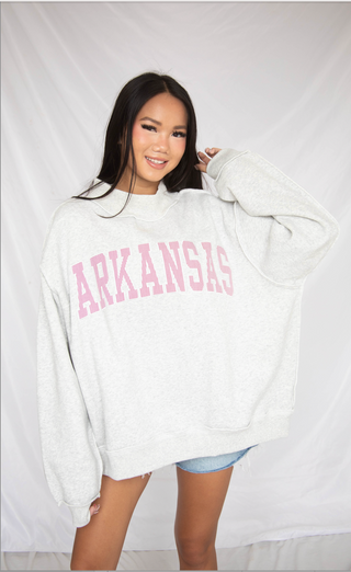 Person wearing a white sweatshirt with 'ARKANSAS' printed in pink on a plain background